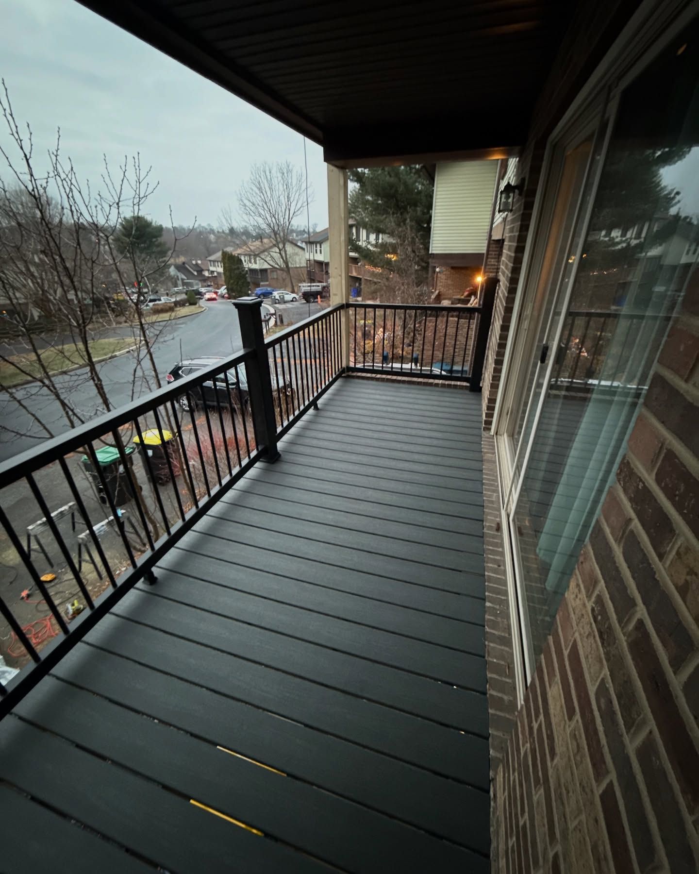 A balcony with dark gray composite decking, black railing, and a view of a street.