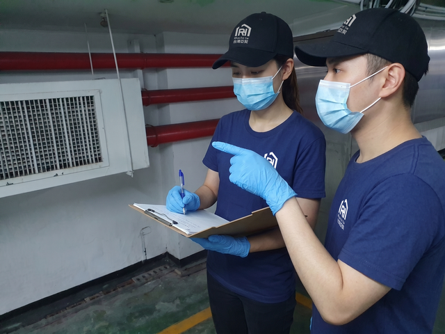 兩名身穿藍色制服、口罩的工人在工業設備旁做筆記。