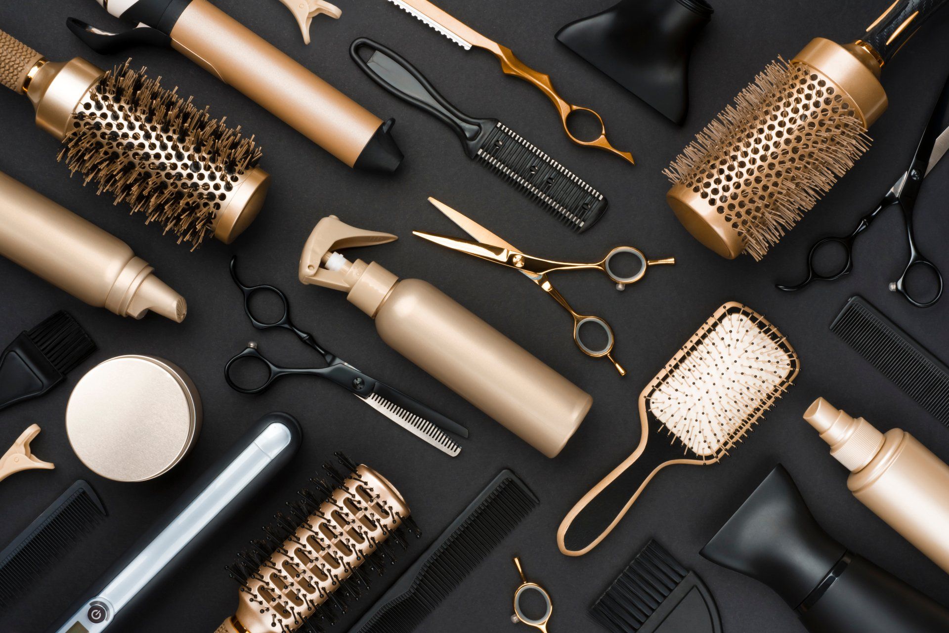A bunch of hair brushes , combs , scissors , and spray bottles on a black surface.