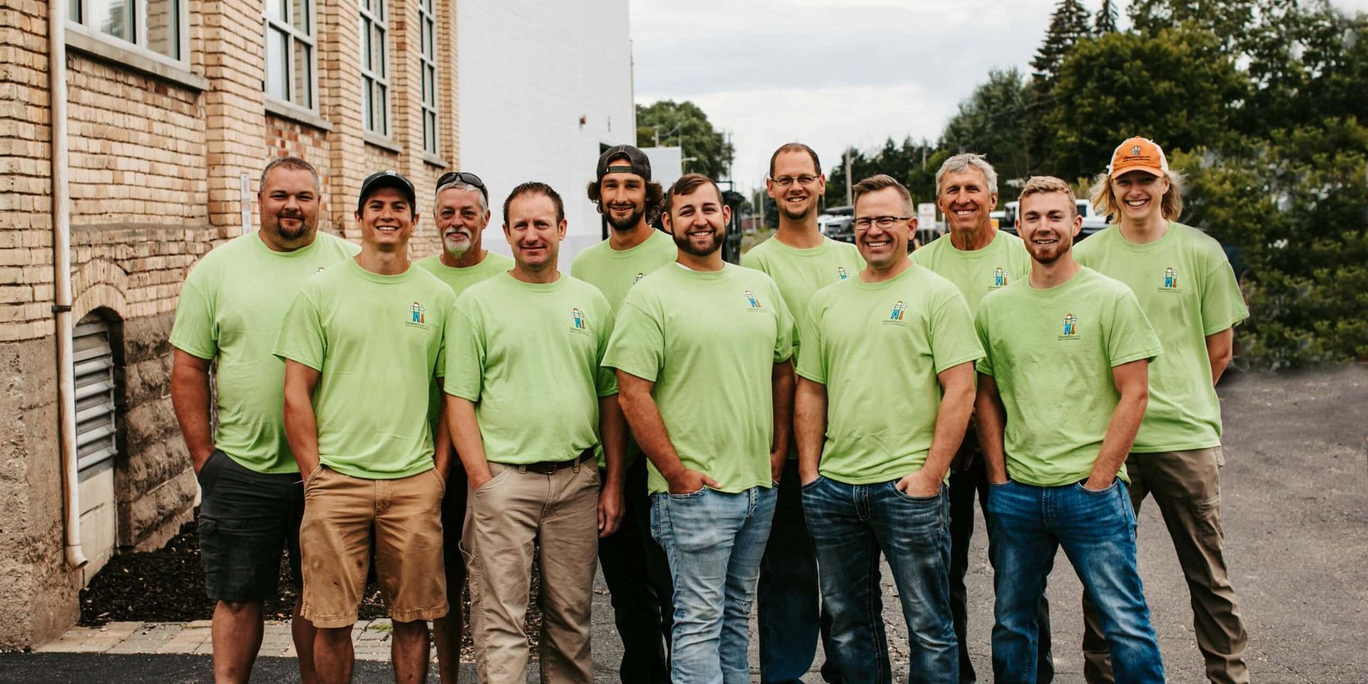 Group of men in lime green t-shirts posing outdoors in front of a brick building.