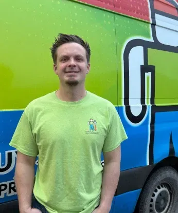 Man in lime green shirt smiles in front of a van with a colorful logo.