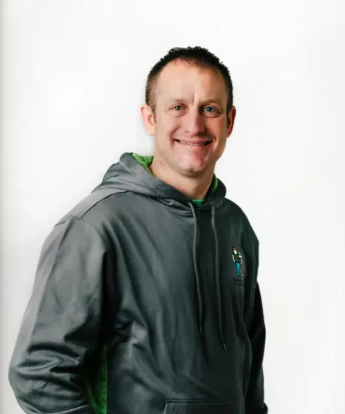 Man in gray hoodie smiling, leaning slightly towards the camera. Green accents on the hood and inside the hoodie. White background.