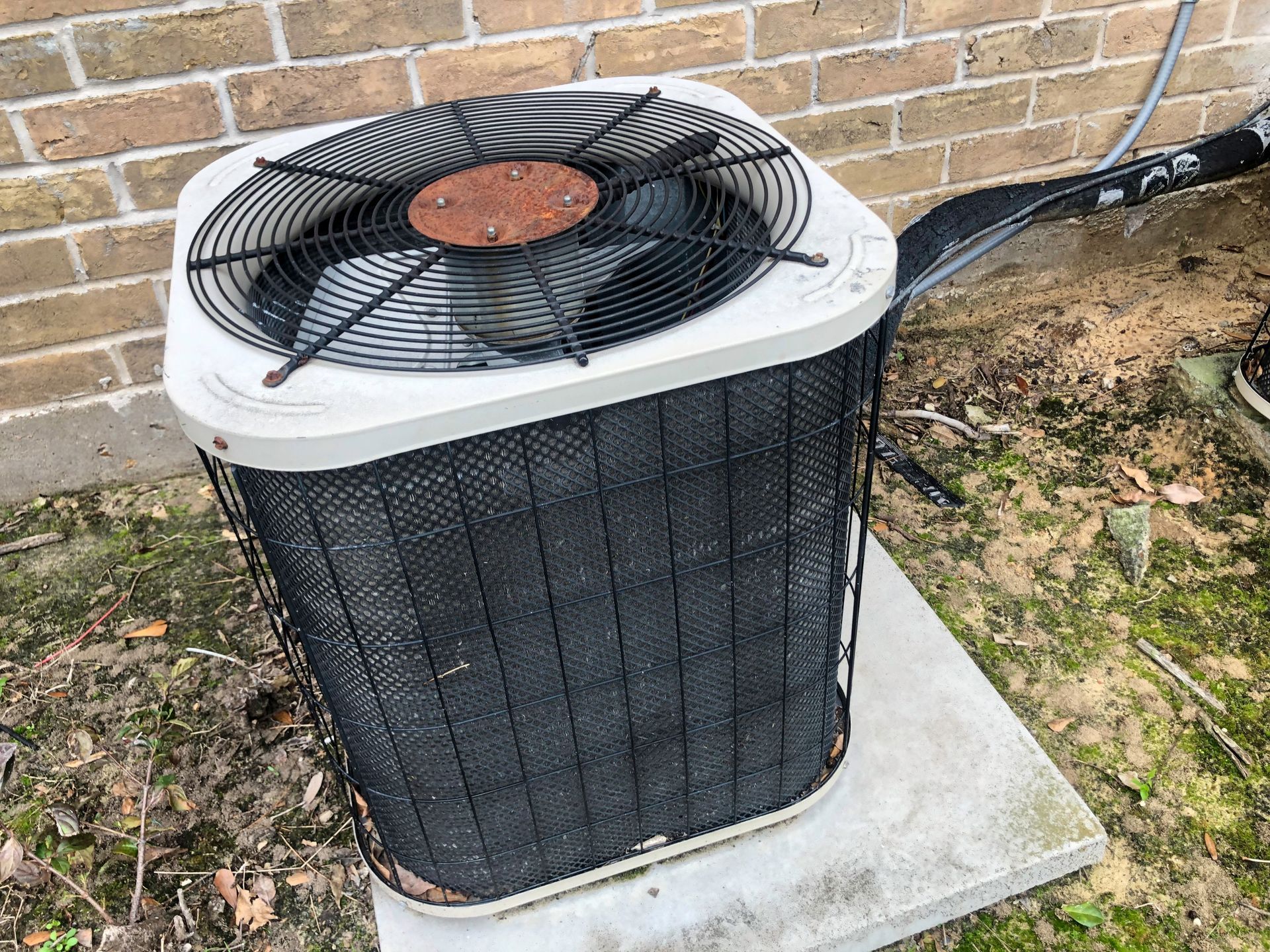 An outdoor air conditioning unit on a concrete pad next to a brick wall.