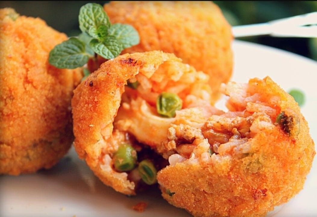 Palline di riso fritte con ripieno di piselli, guarnite con menta e servite su un piatto bianco.