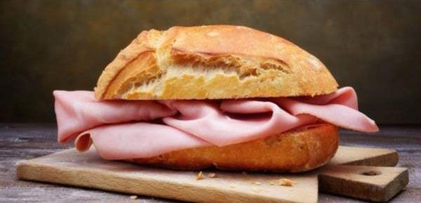 Un panino al prosciutto su un tagliere di legno.