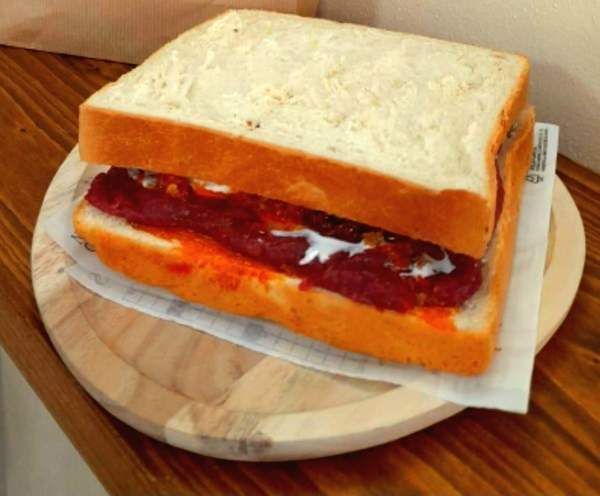 Panino su un tagliere di legno. Pane tagliato spesso circonda un ripieno scuro con salsa rossa e besciamella.