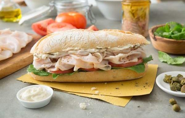 Panino con tacchino, pomodori, lattuga e maionese su carta gialla.