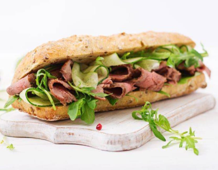 Panino con roast beef, rucola e cetriolo su un tagliere di legno.