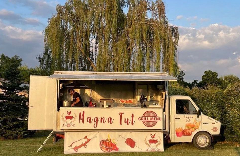 Il food truck "Magna Tut" parcheggiato all'aperto, con una persona che lavora all'interno.