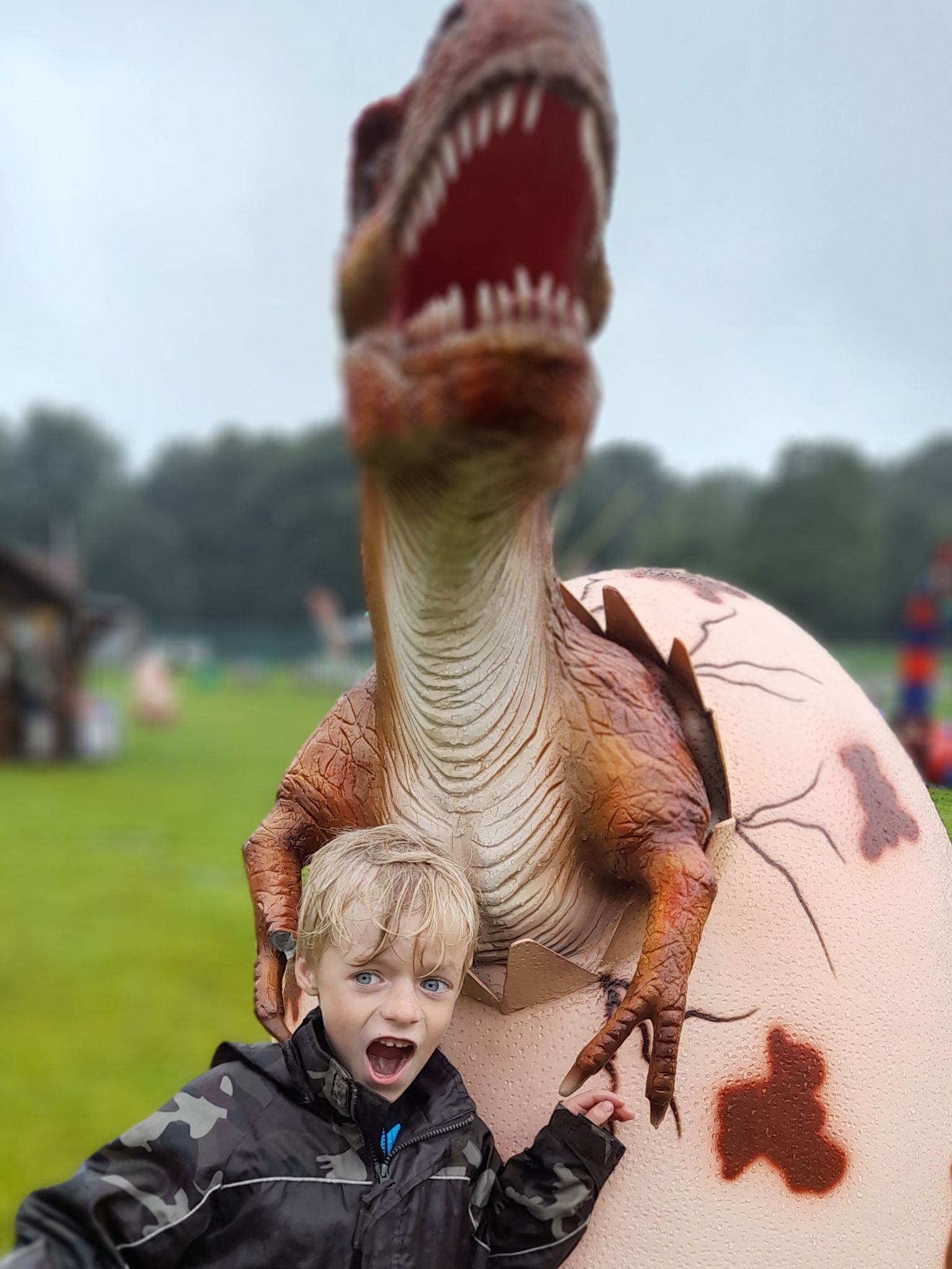 A young boy is standing next to a statue of a dinosaur coming out of an egg.