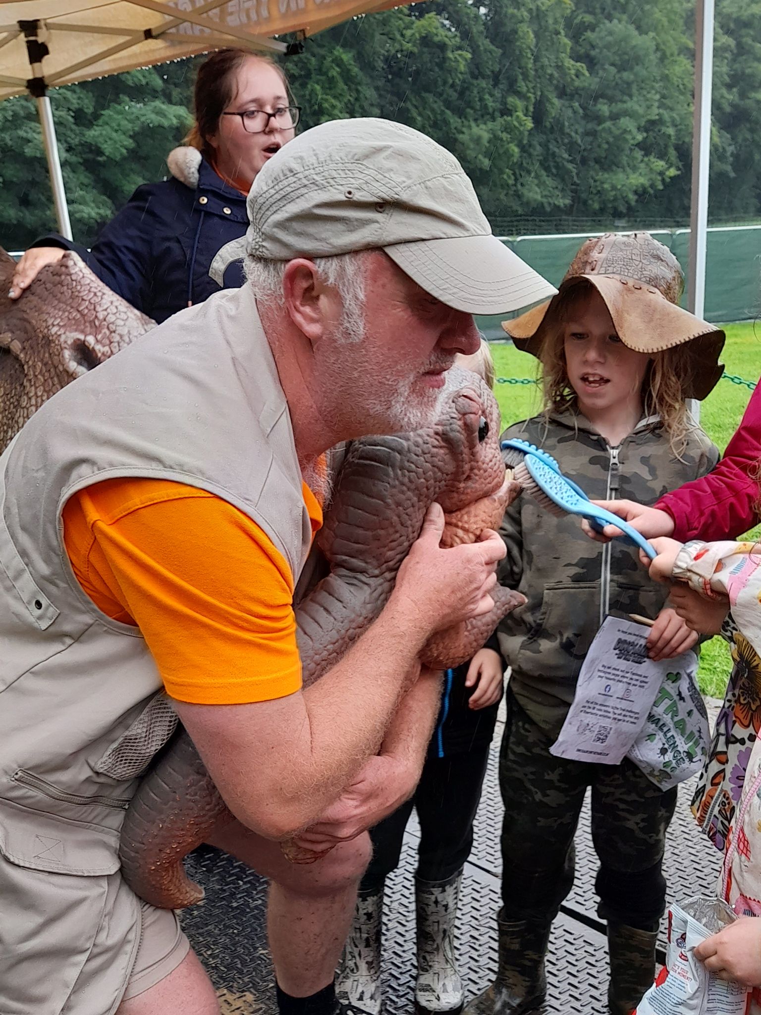 A man is holding a lizard in his arms while a group of children look on.