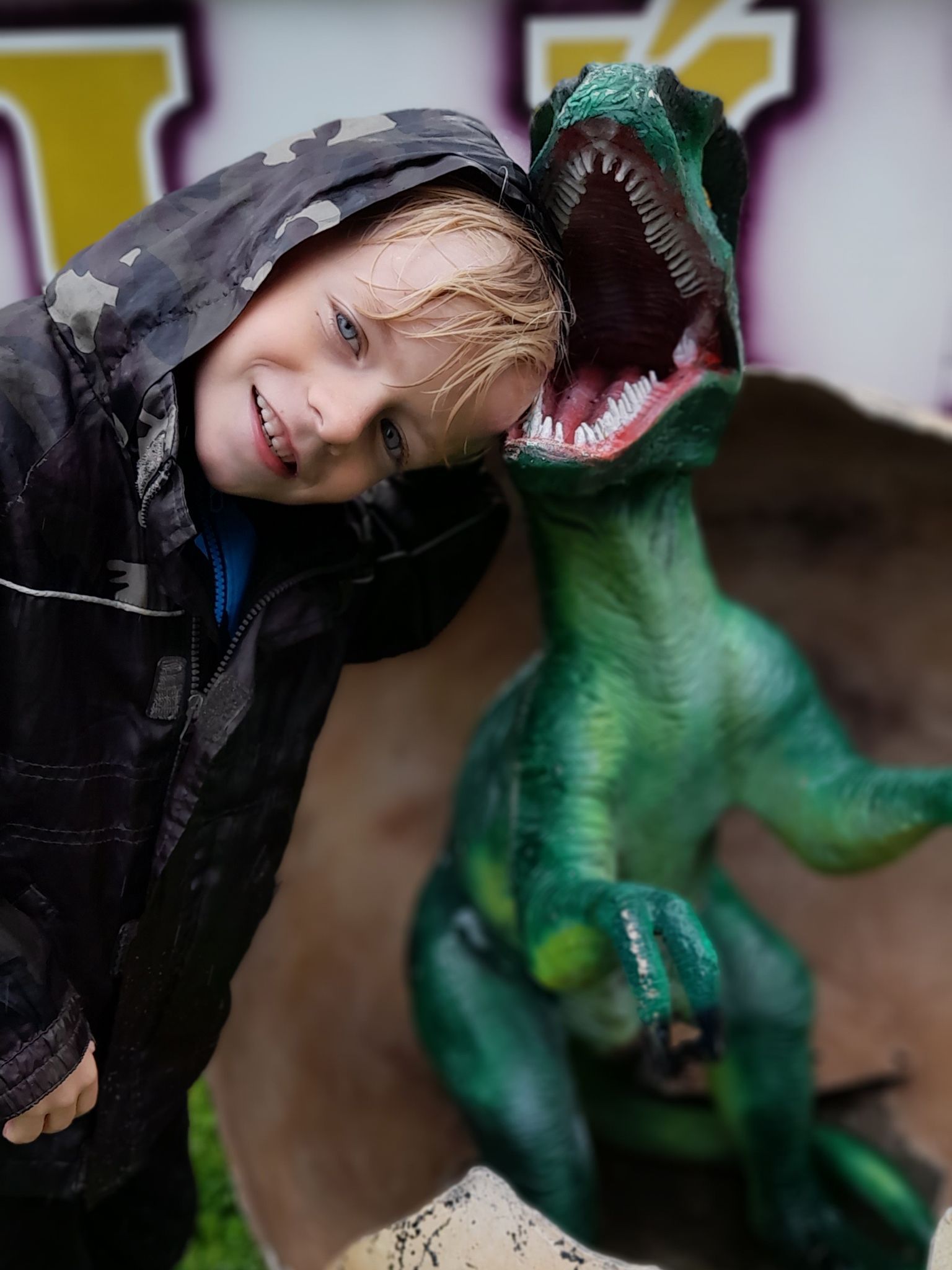 A young boy standing next to a green dinosaur statue