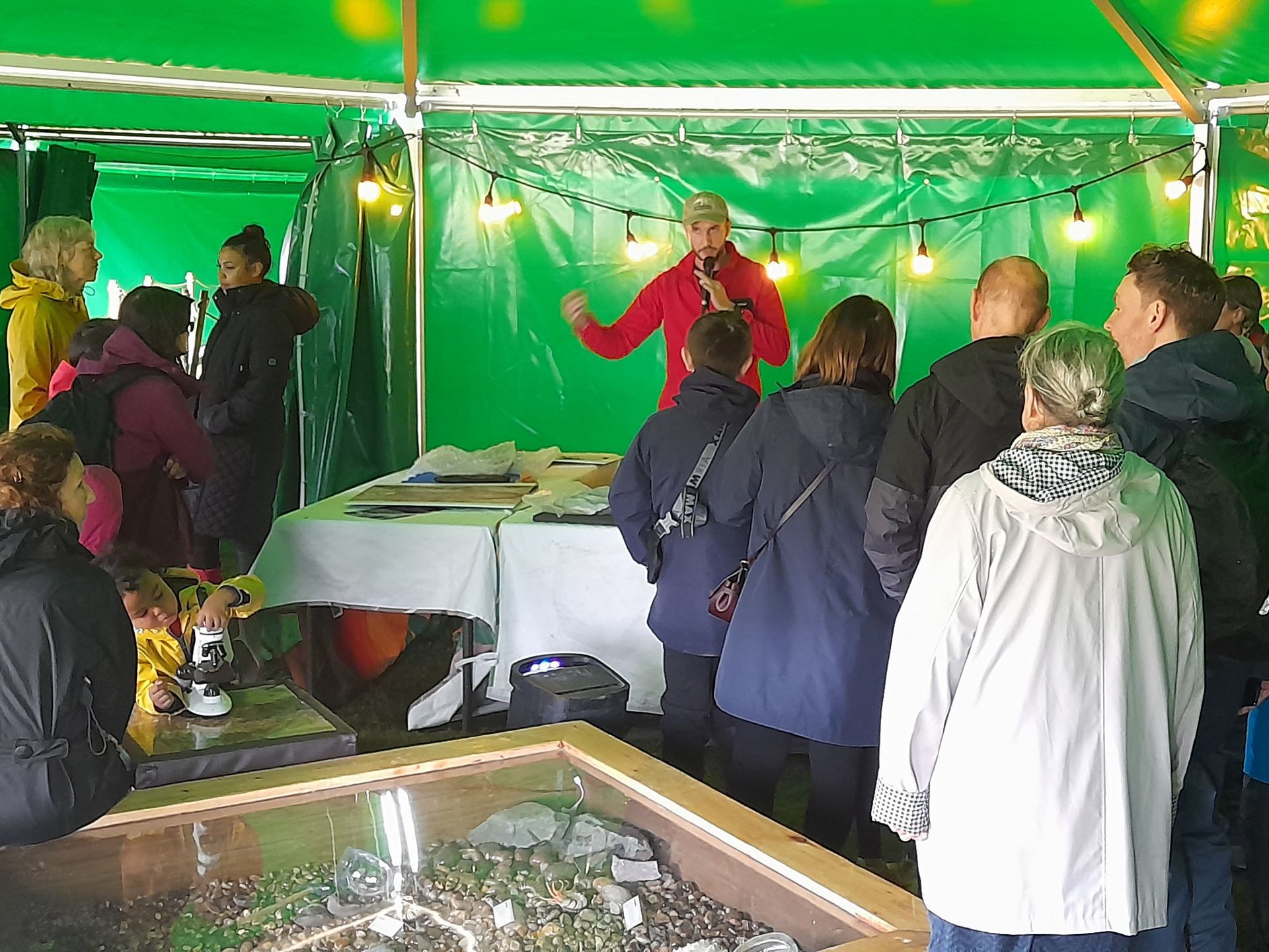 A group of people are standing around a table under a green tent.