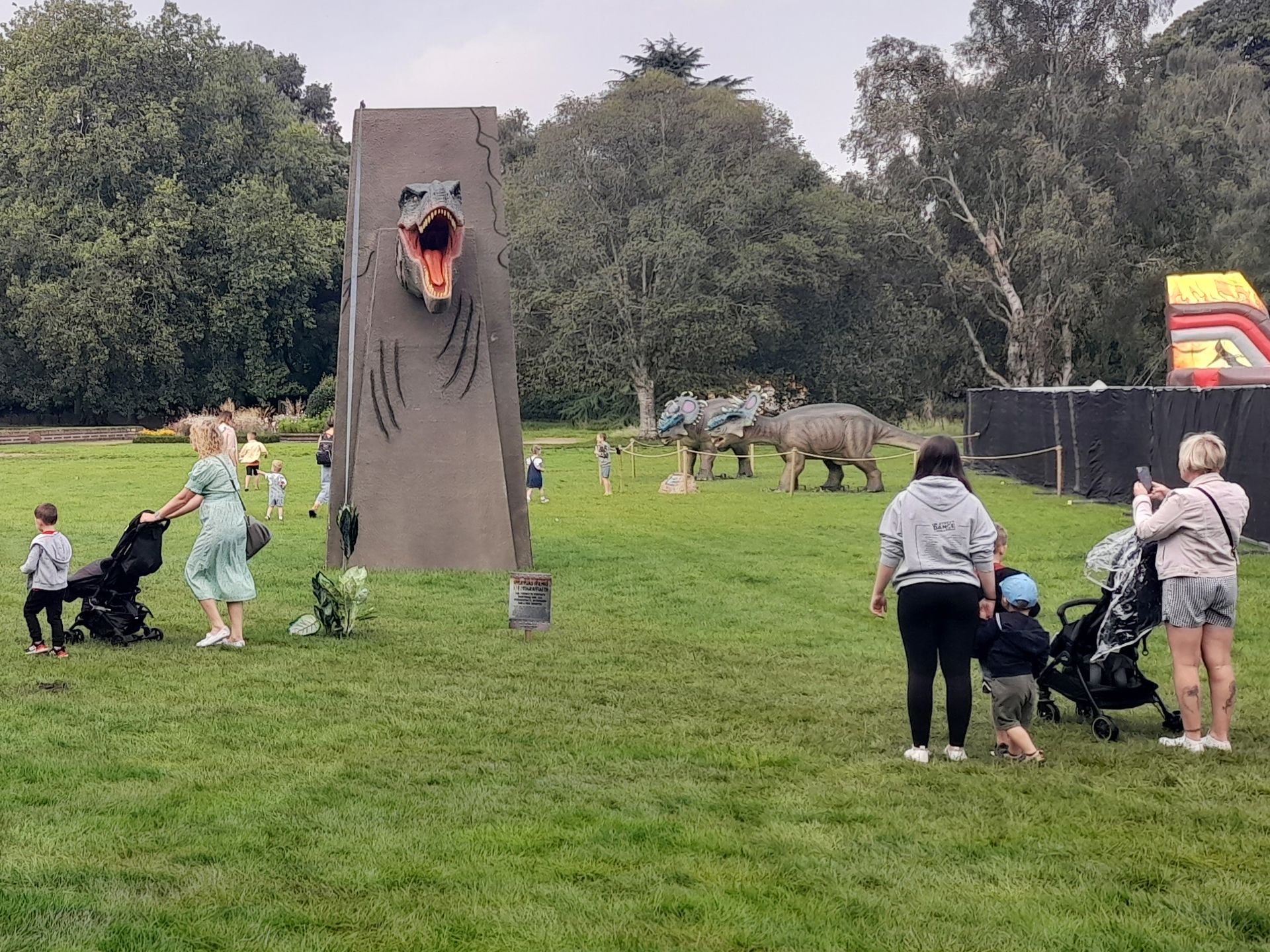 A group of people are standing in a grassy field in front of a dinosaur model.