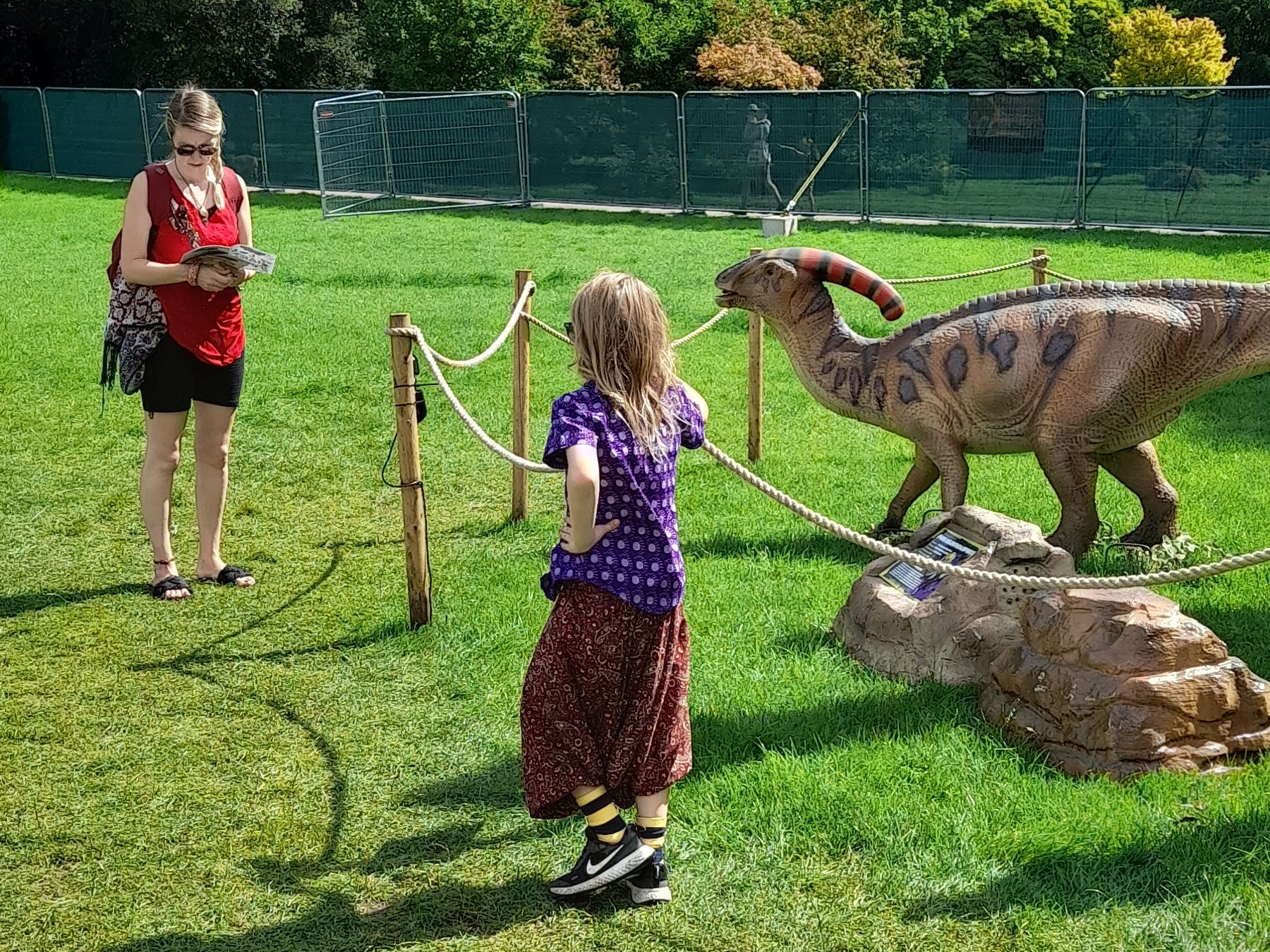 A woman and a little girl are standing in front of a dinosaur model.