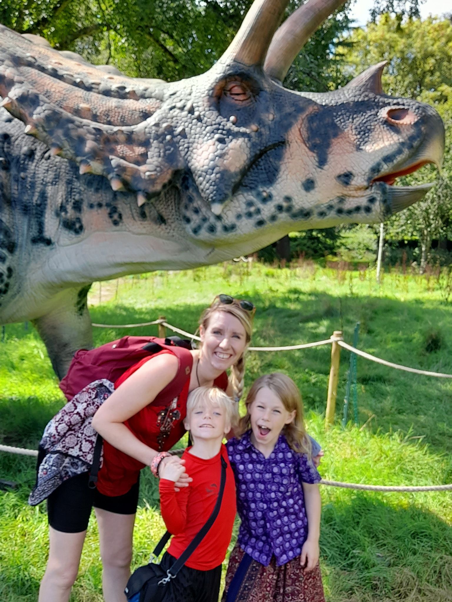 A woman and two children are posing for a picture in front of a dinosaur model.