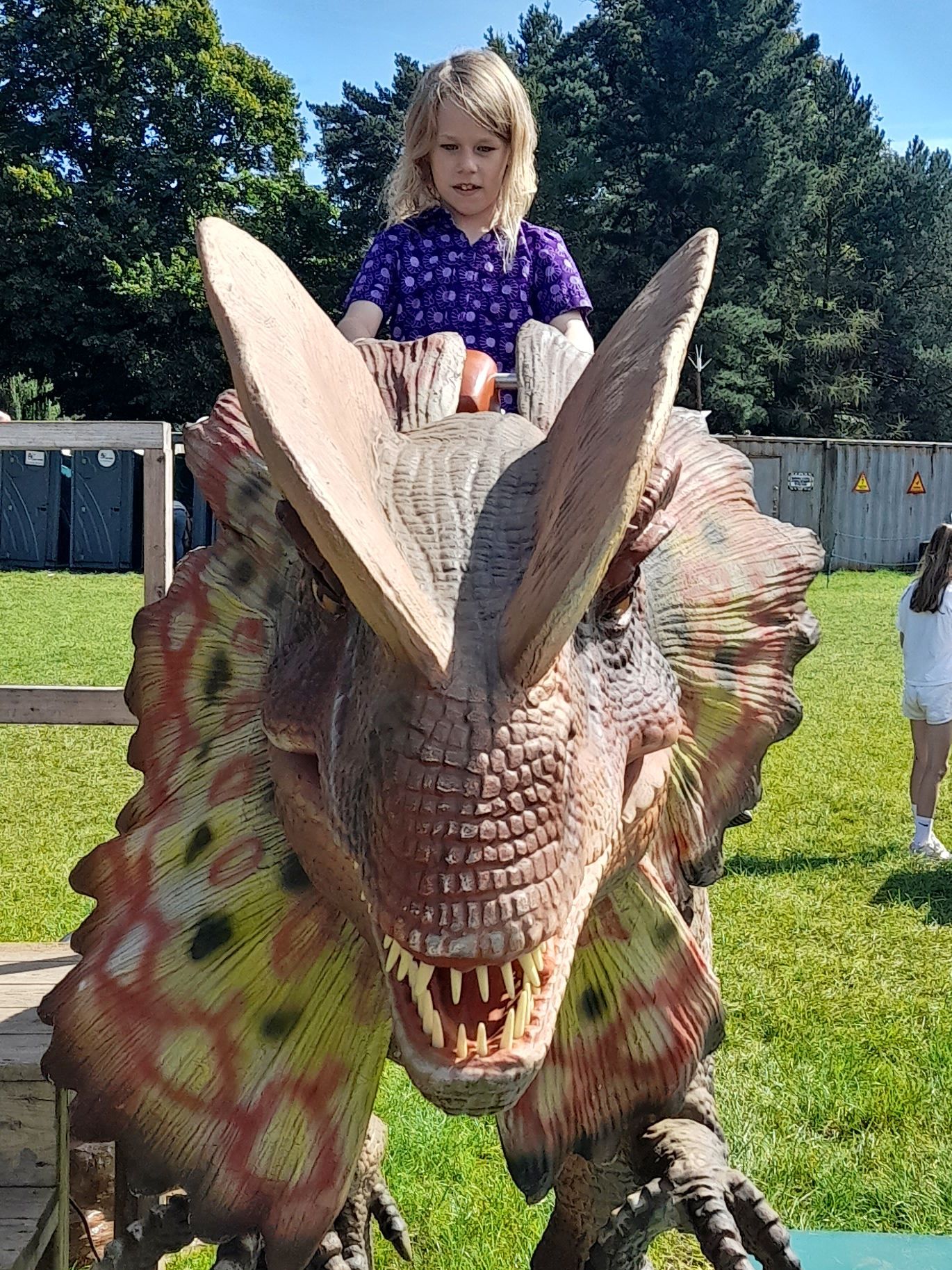 A little girl is riding on the back of a dinosaur model.