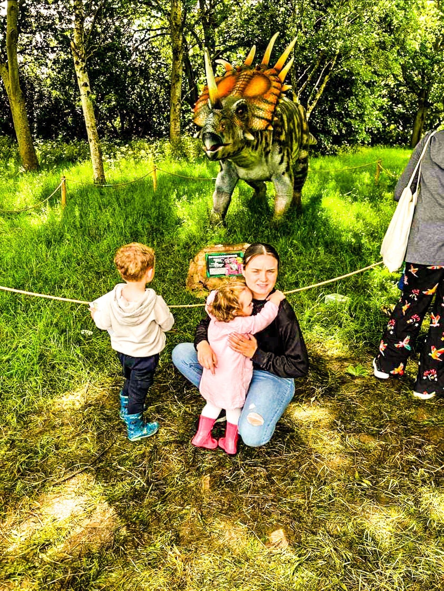 A woman is kneeling down with two children in front of a dinosaur statue.