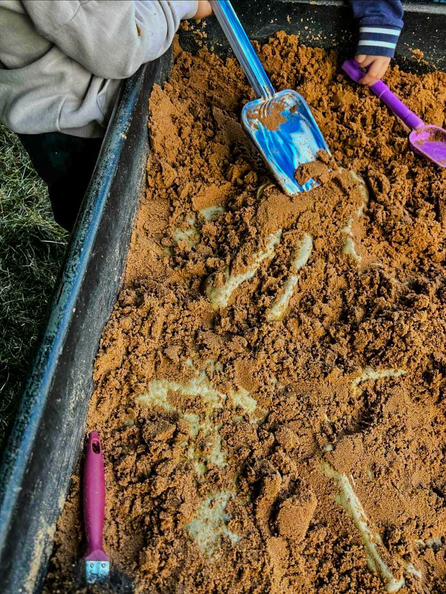 A child is playing in a sandbox with a shovel.