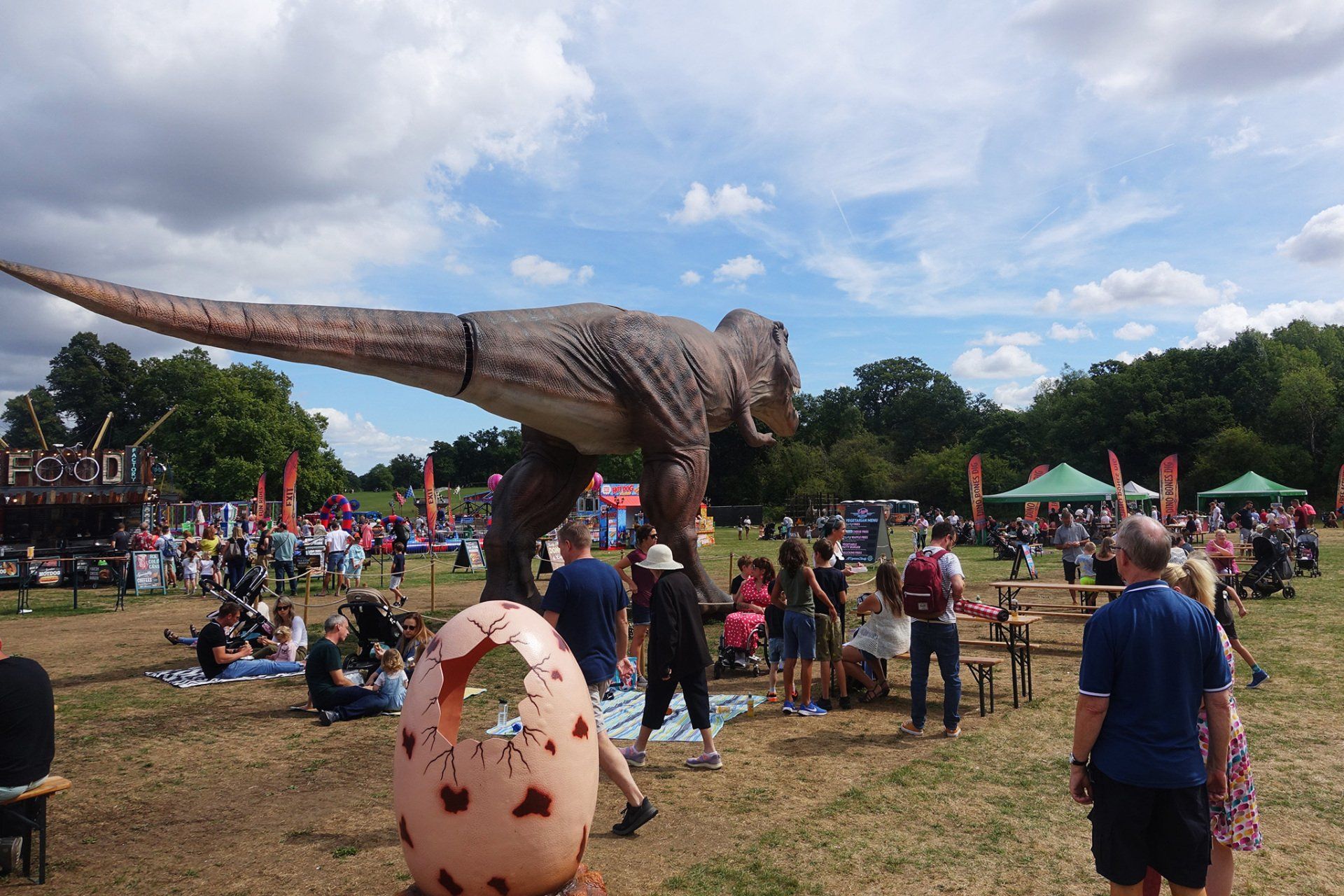 A statue of a dinosaur is in a field with people.