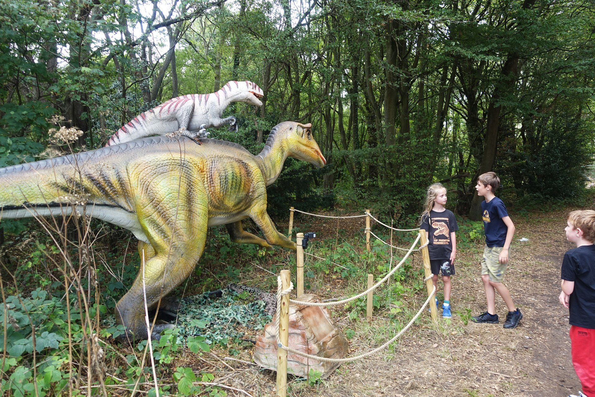 A group of children are standing in front of a model of a dinosaur.