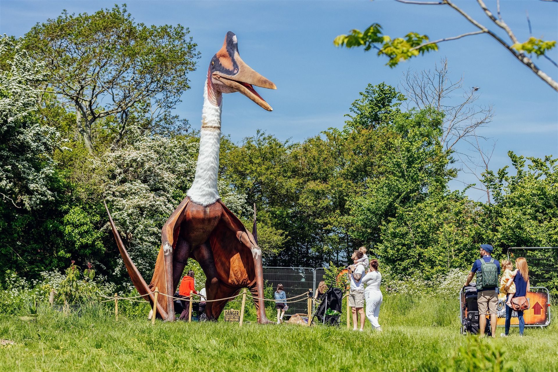 A group of people are standing around a large dinosaur statue in a field.