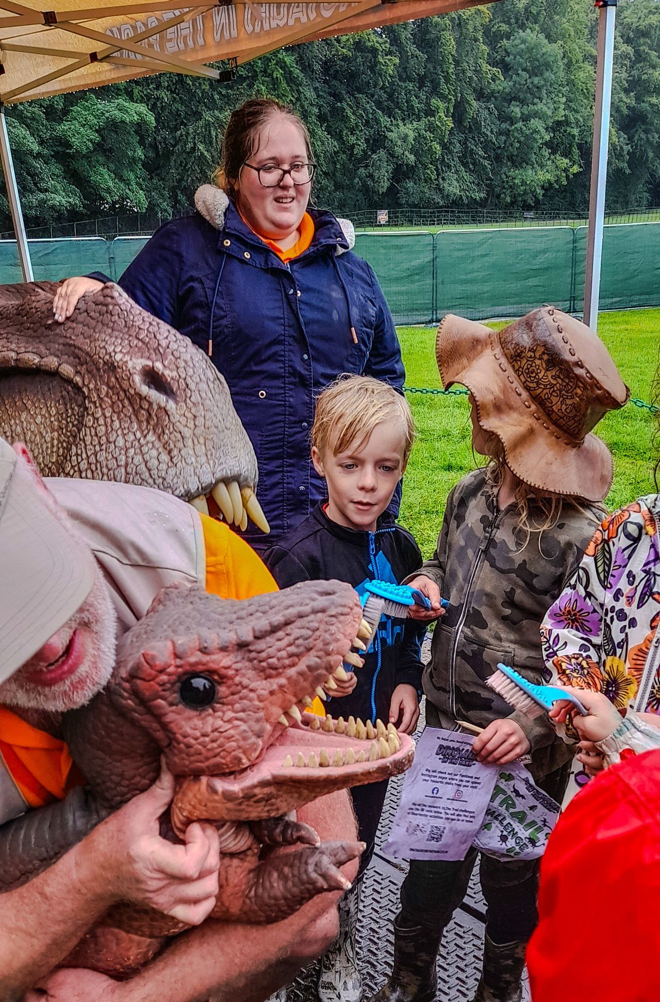 A group of people are standing around a man in a dinosaur costume holding a stuffed animal.