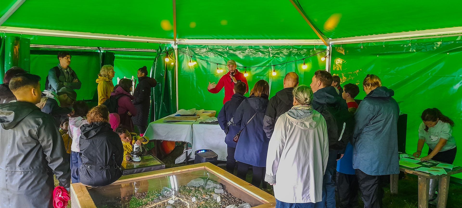 A group of people are standing around a table under a green tent.