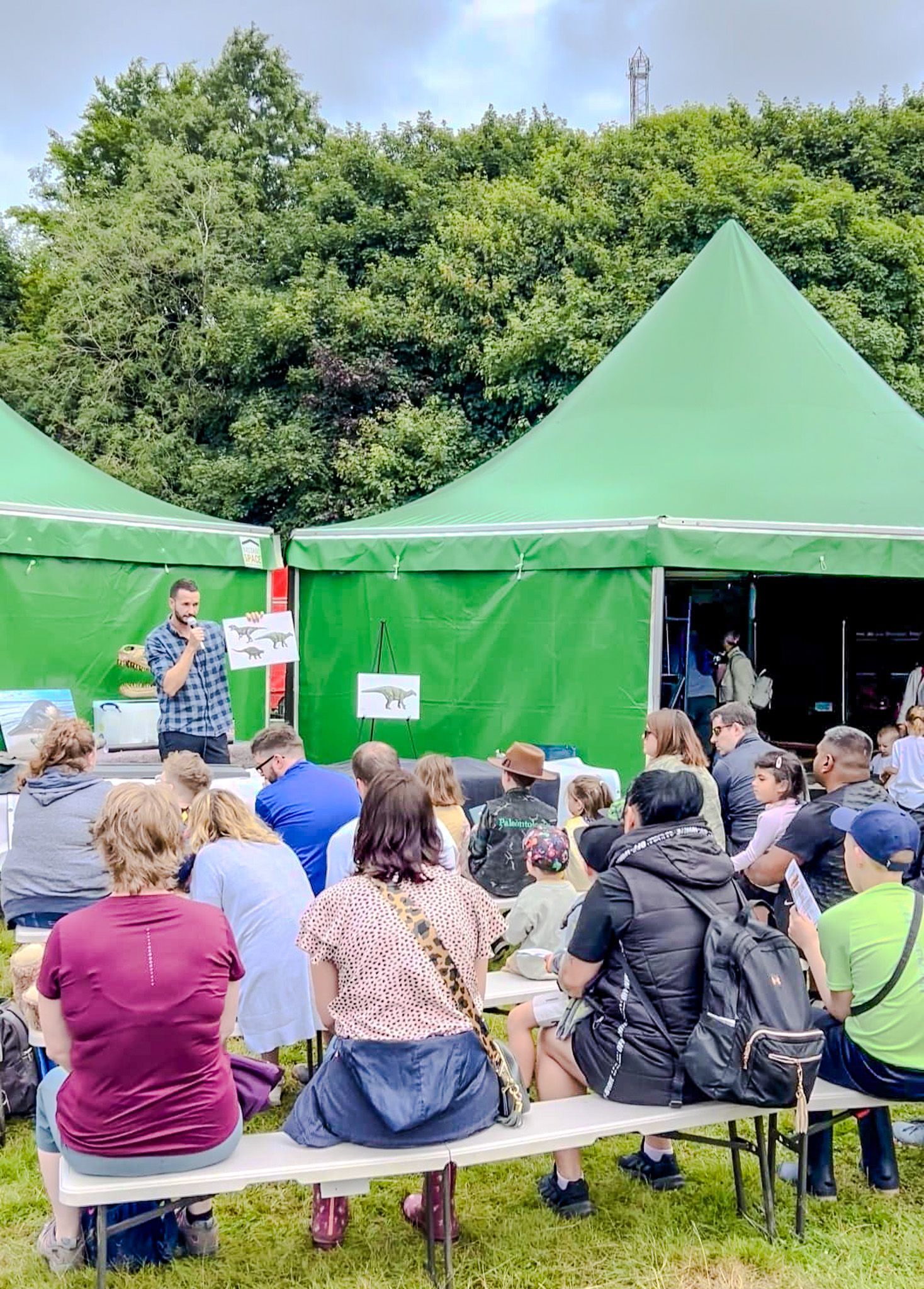 A group of people are sitting on benches in front of a green tent.