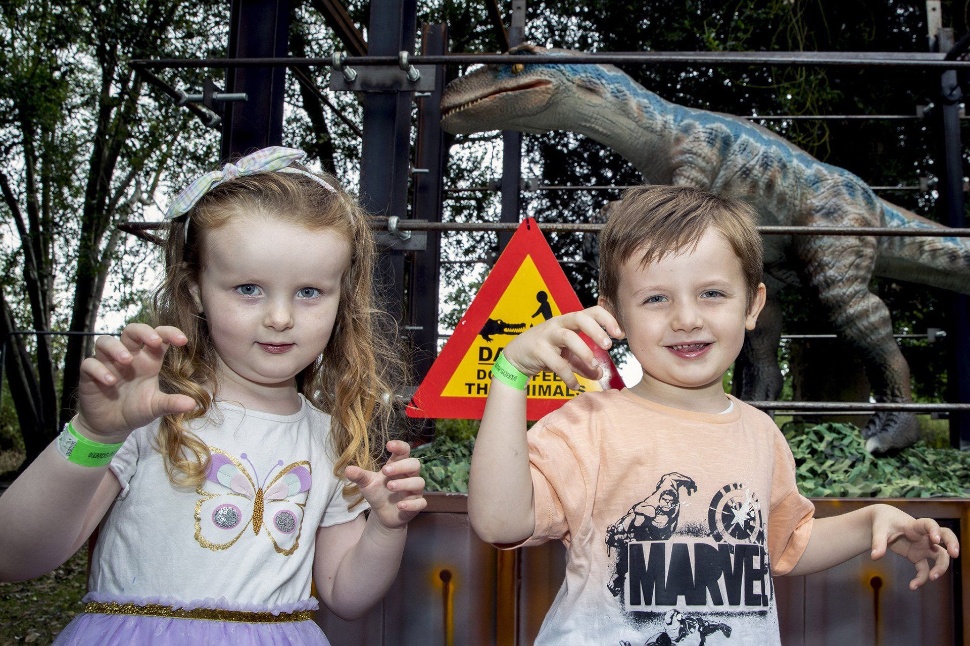 A boy and a girl are standing next to each other in front of a dinosaur.