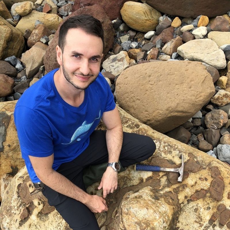 A man in a blue shirt is sitting on a rock with a hammer