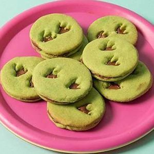 A pink plate topped with green cookies with chocolate filling.