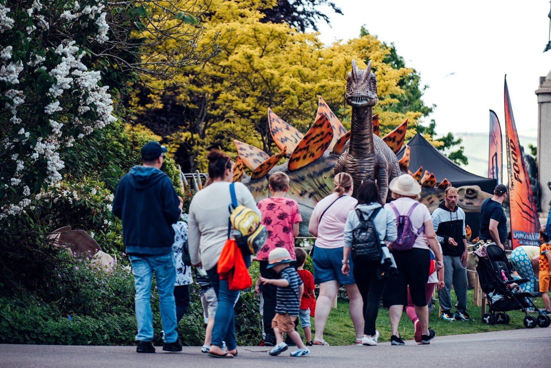 A group of people are walking in front of a statue of a dinosaur.