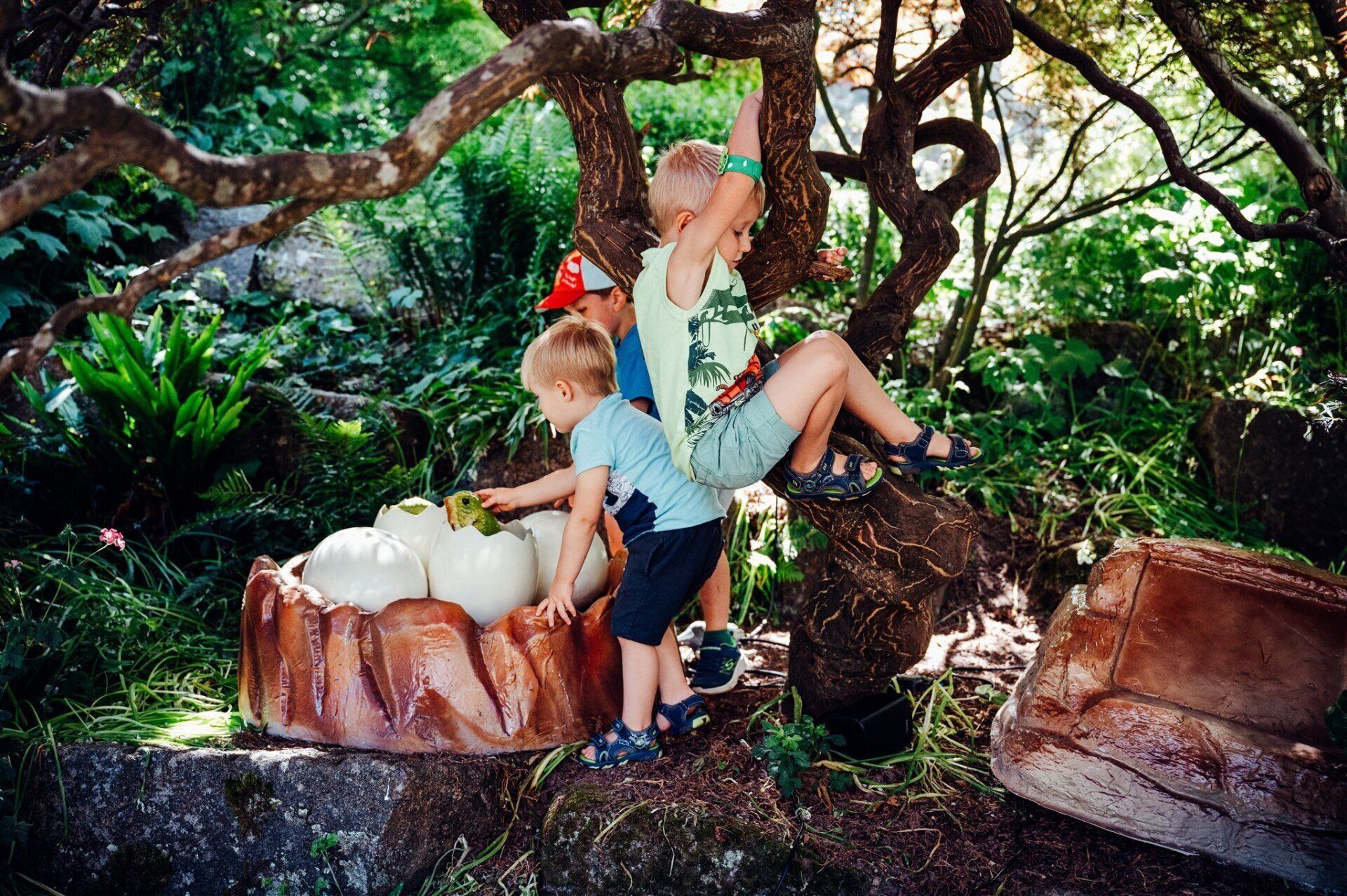 Two young boys are playing with a dinosaur statue in the woods