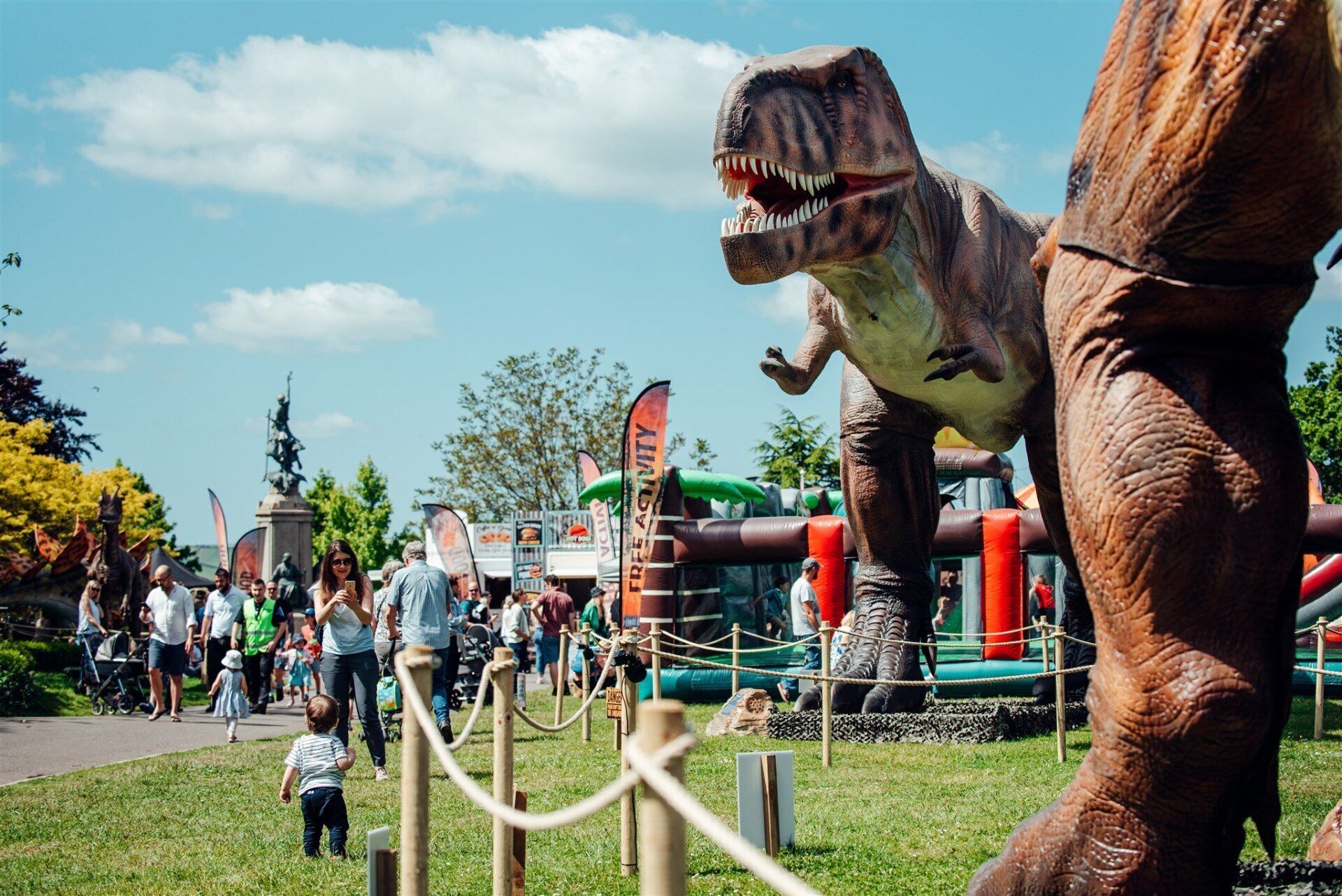A statue of a dinosaur is standing in a park.