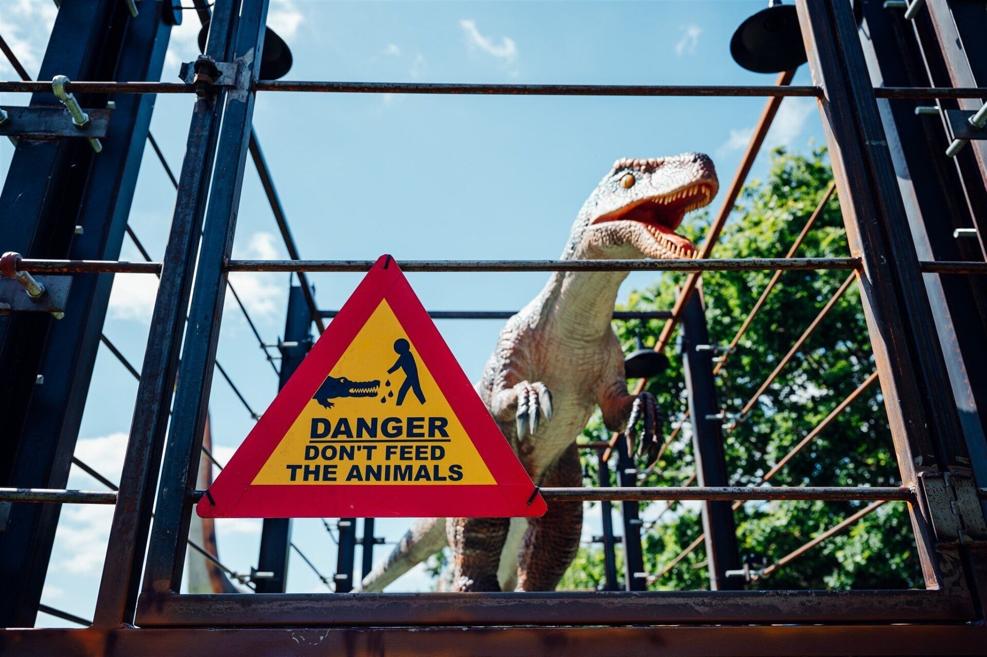 A dinosaur is behind a fence with a sign that says danger don't feed the animals.