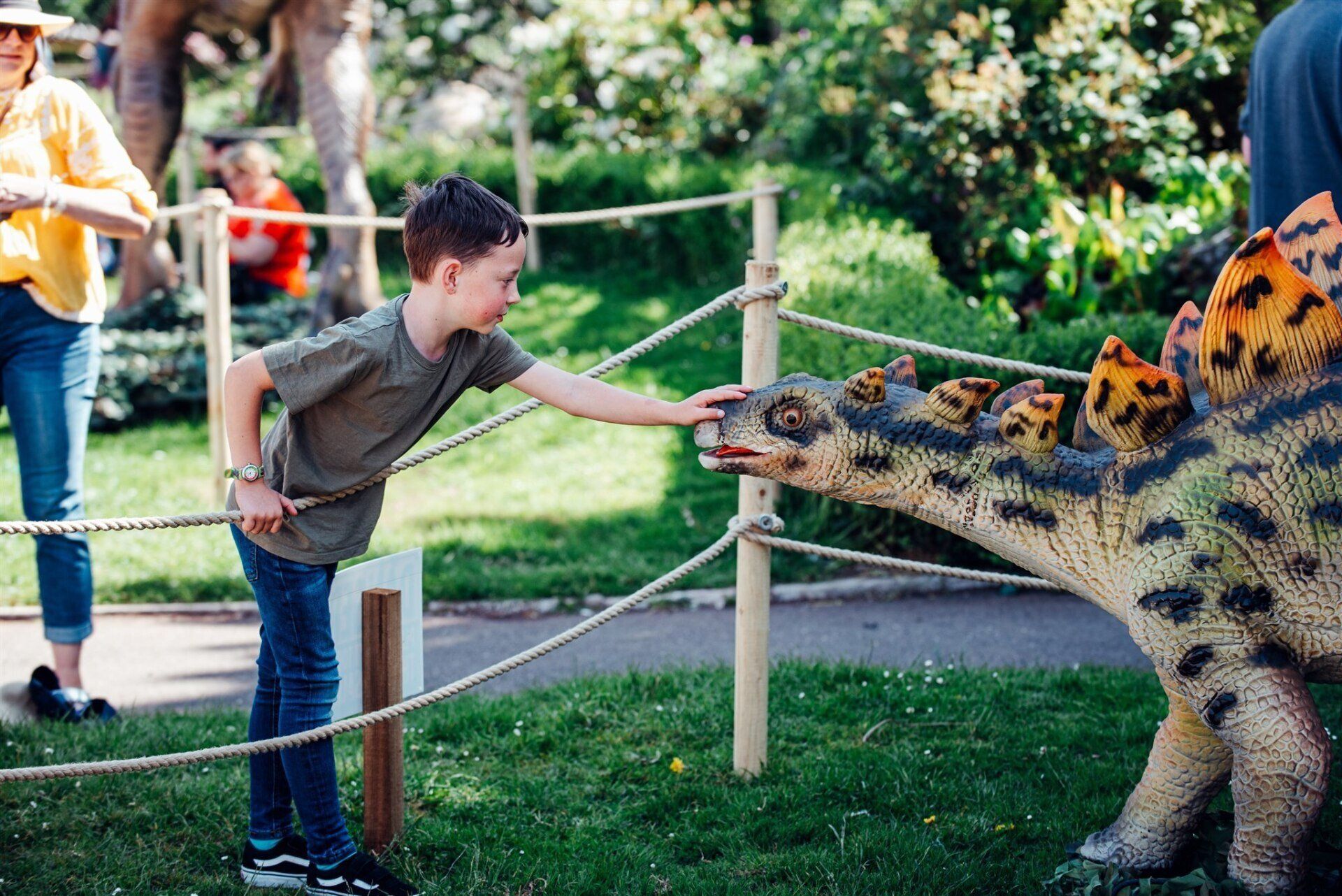 A young boy is petting a dinosaur model in a park.