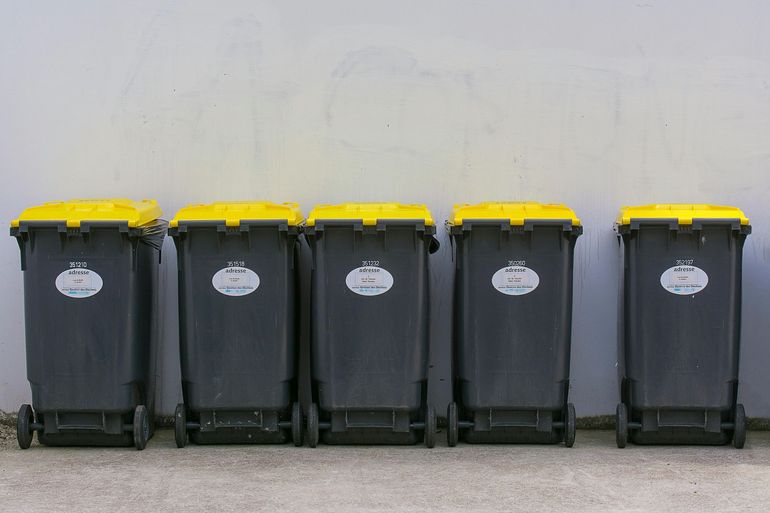 Five black recycling bins with yellow lids against a light gray wall.