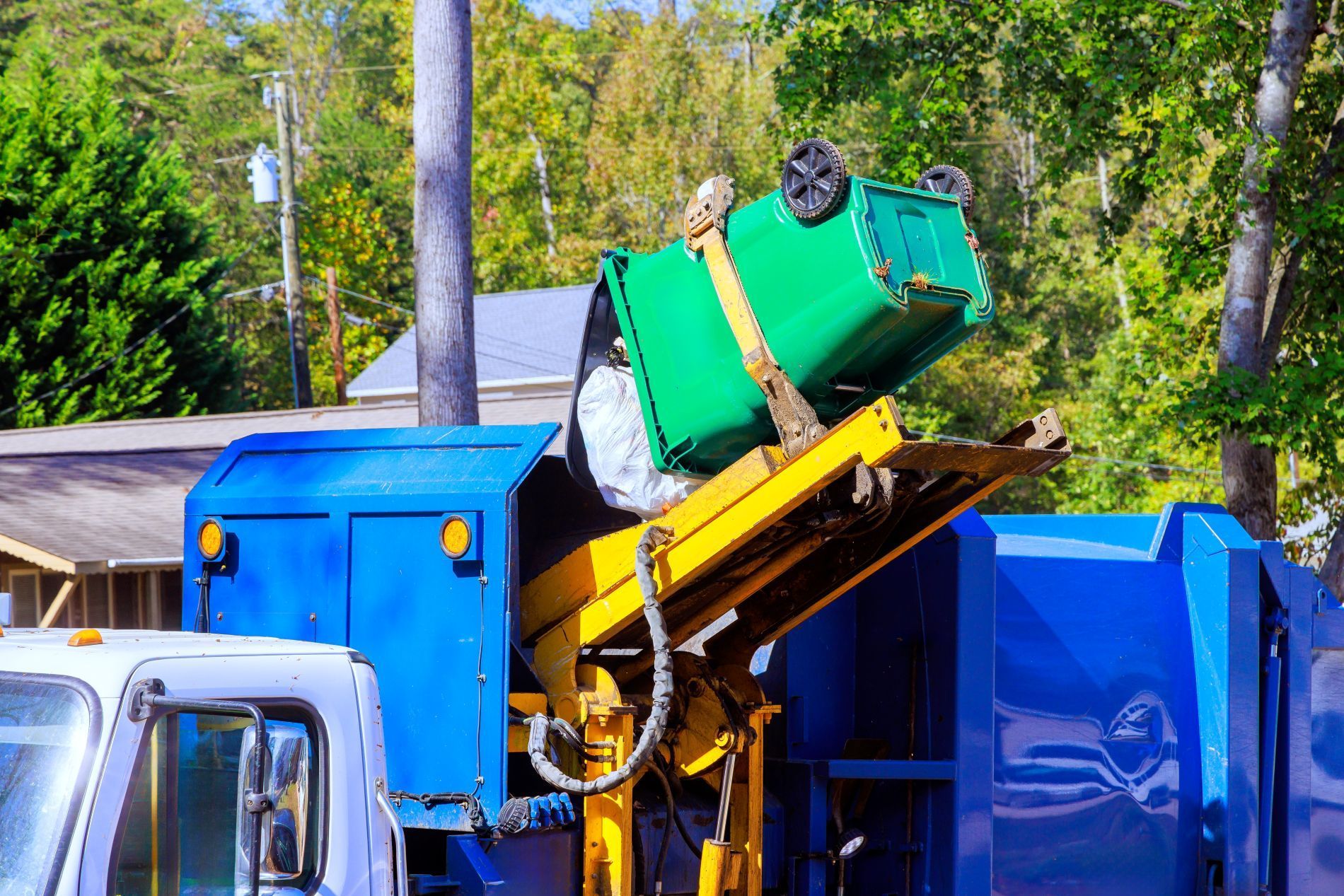 A green trash bin being emptied into a blue garbage truck by a mechanical arm.