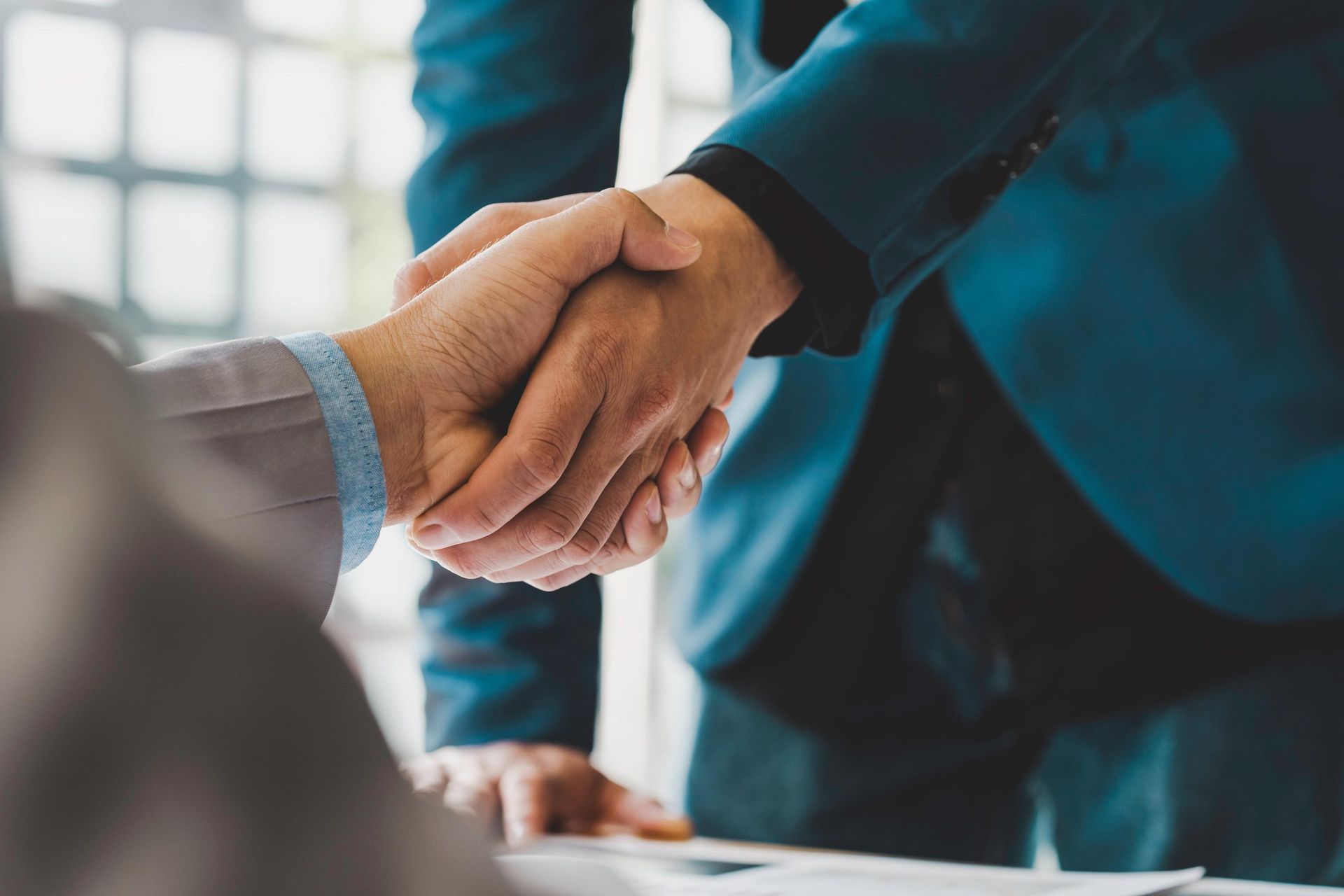 Two people in business suits shaking hands across a table