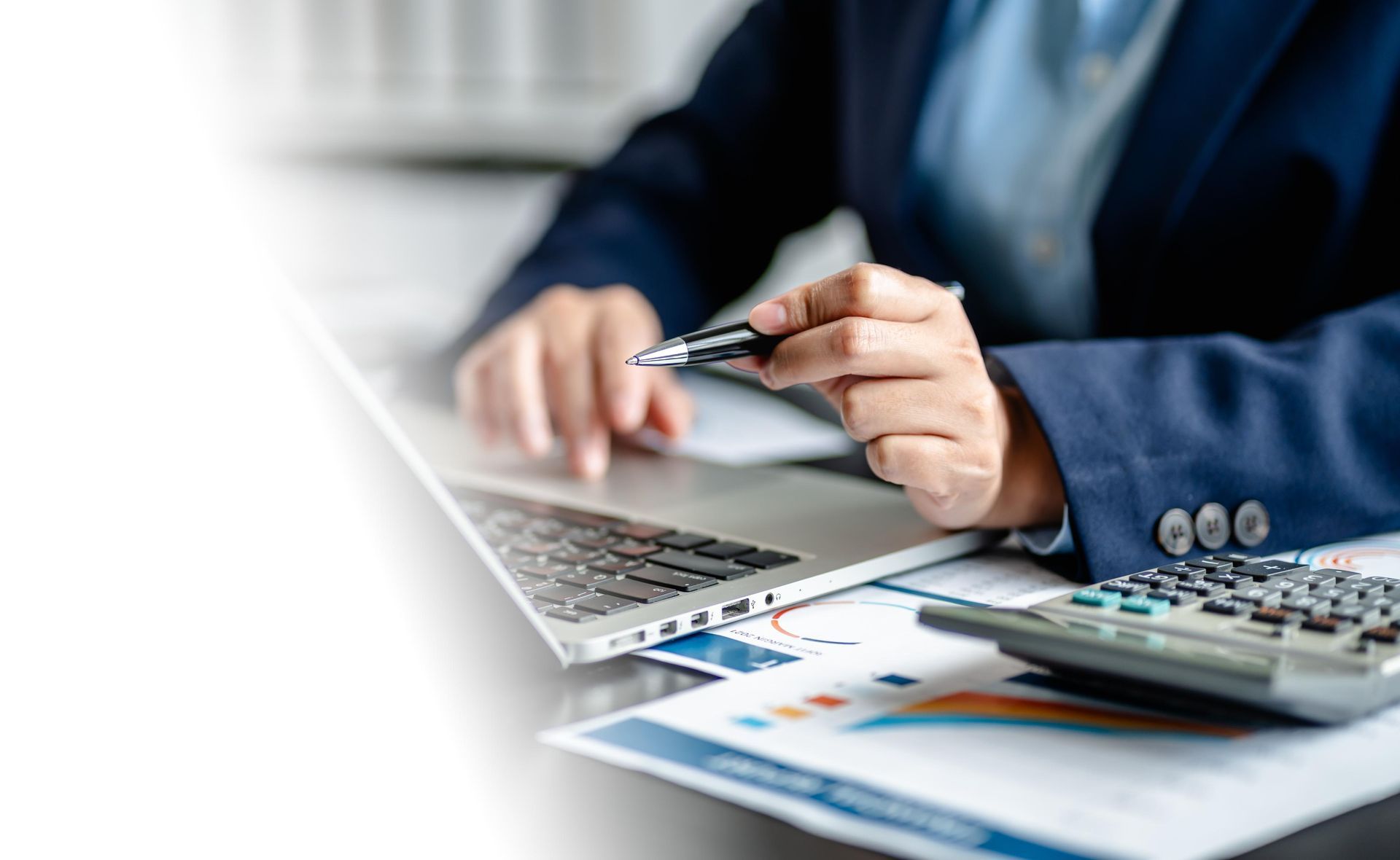 Businessperson reviewing laptop with calculator, pen, and financial charts on a desk
