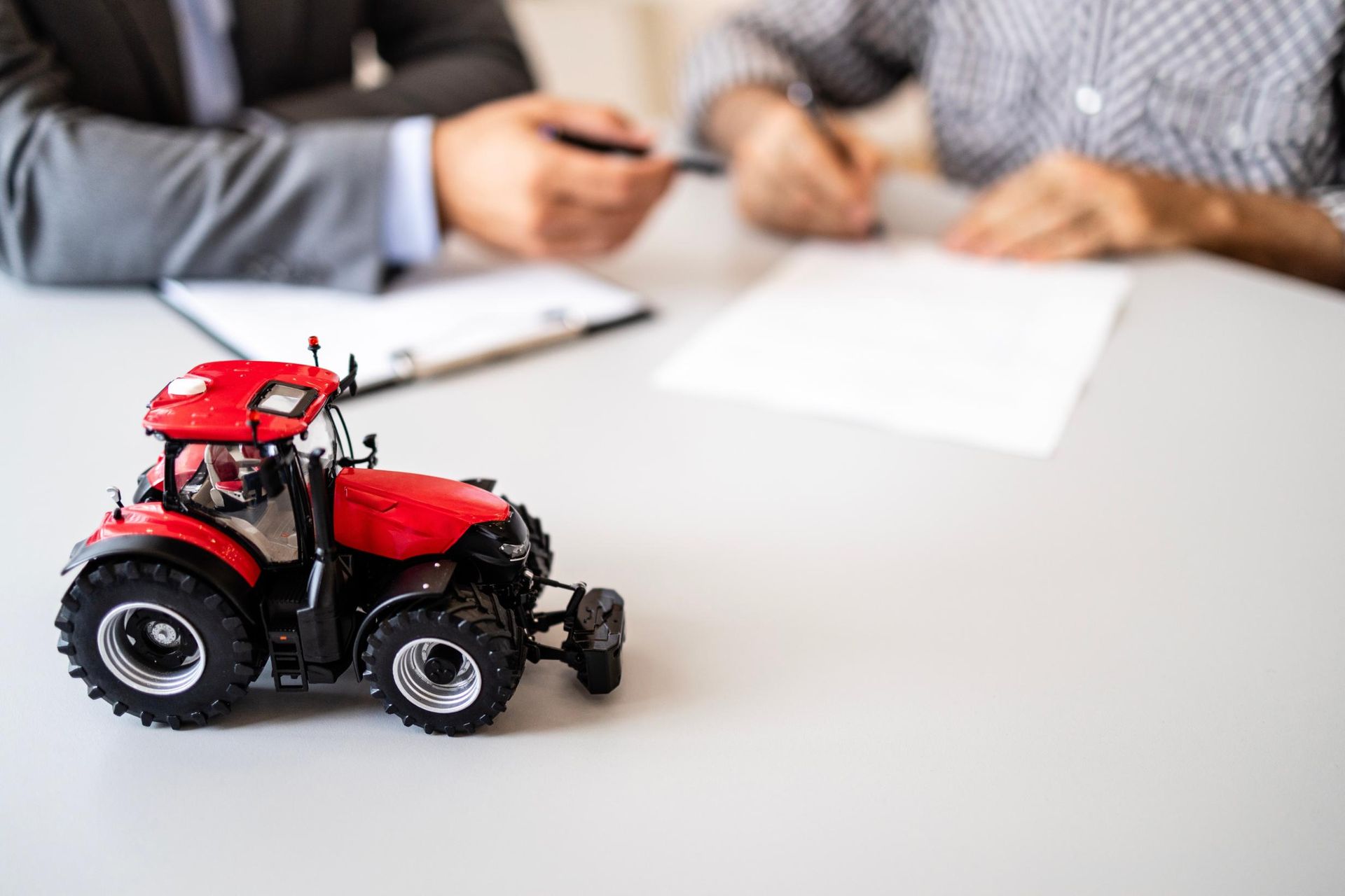 Red toy tractor on a desk with people blurred in the background during a meeting