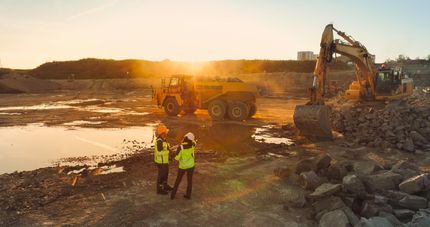 Workers and heavy machinery at a rocky construction site at sunset