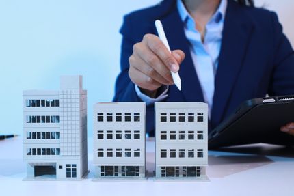 Businessperson pointing at miniature office buildings with a pen and clipboard