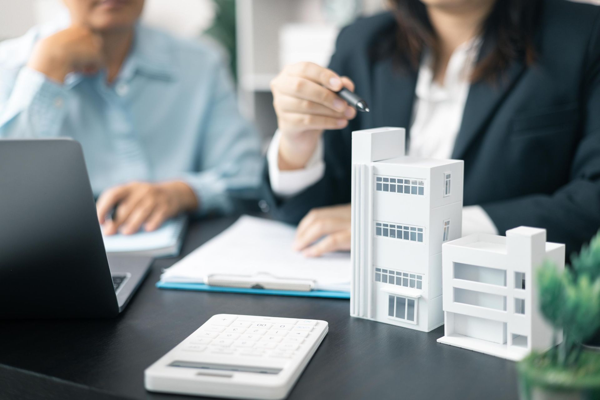Business meeting with people discussing a white architectural model beside a laptop and notebook