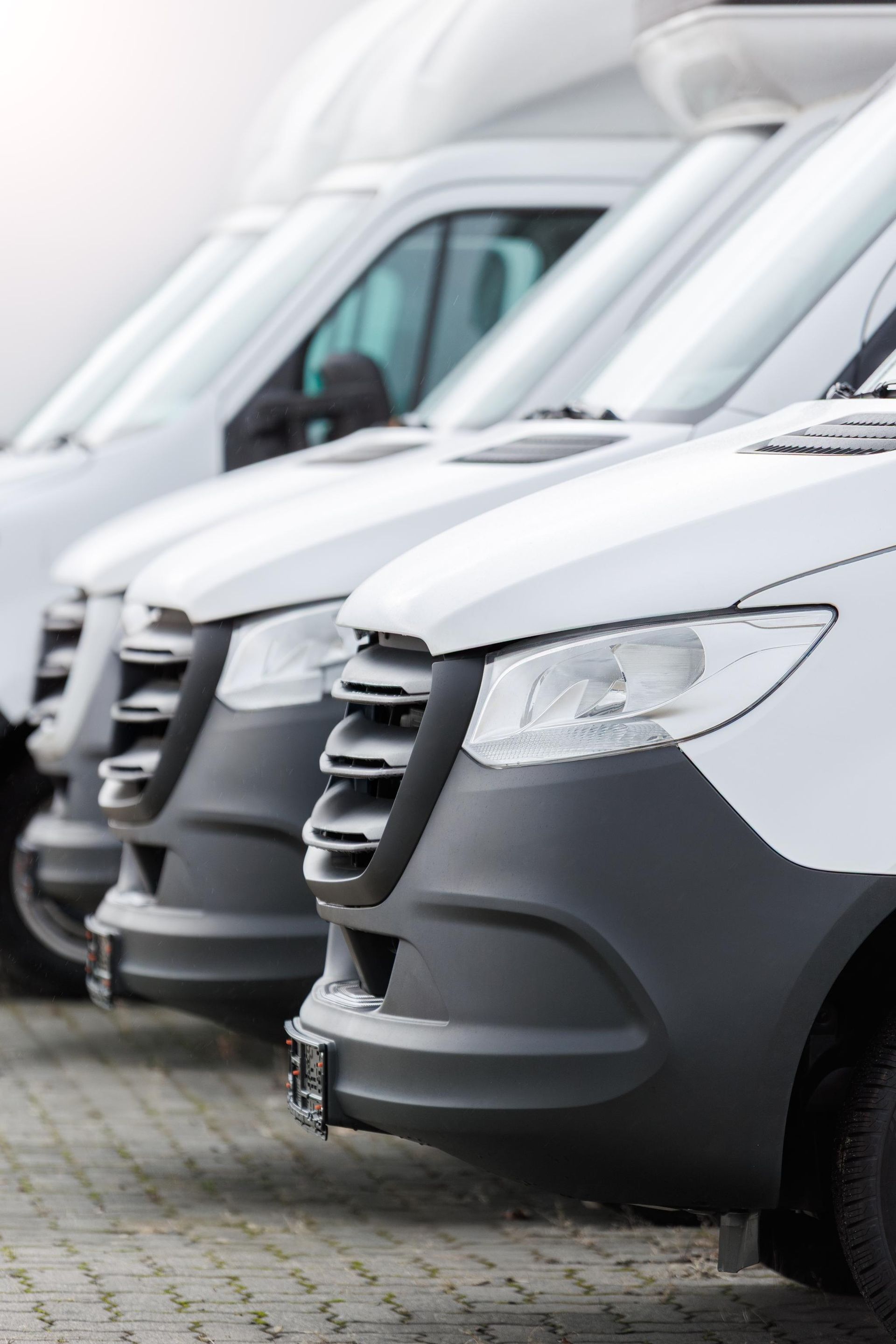Row of white delivery vans parked tightly in a lot, front view