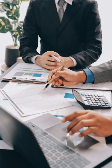 Business meeting with hands reviewing charts, calculator, and laptop on a desk