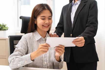 Woman in striped blouse smiling at a document while a colleague in a black suit stands beside her.