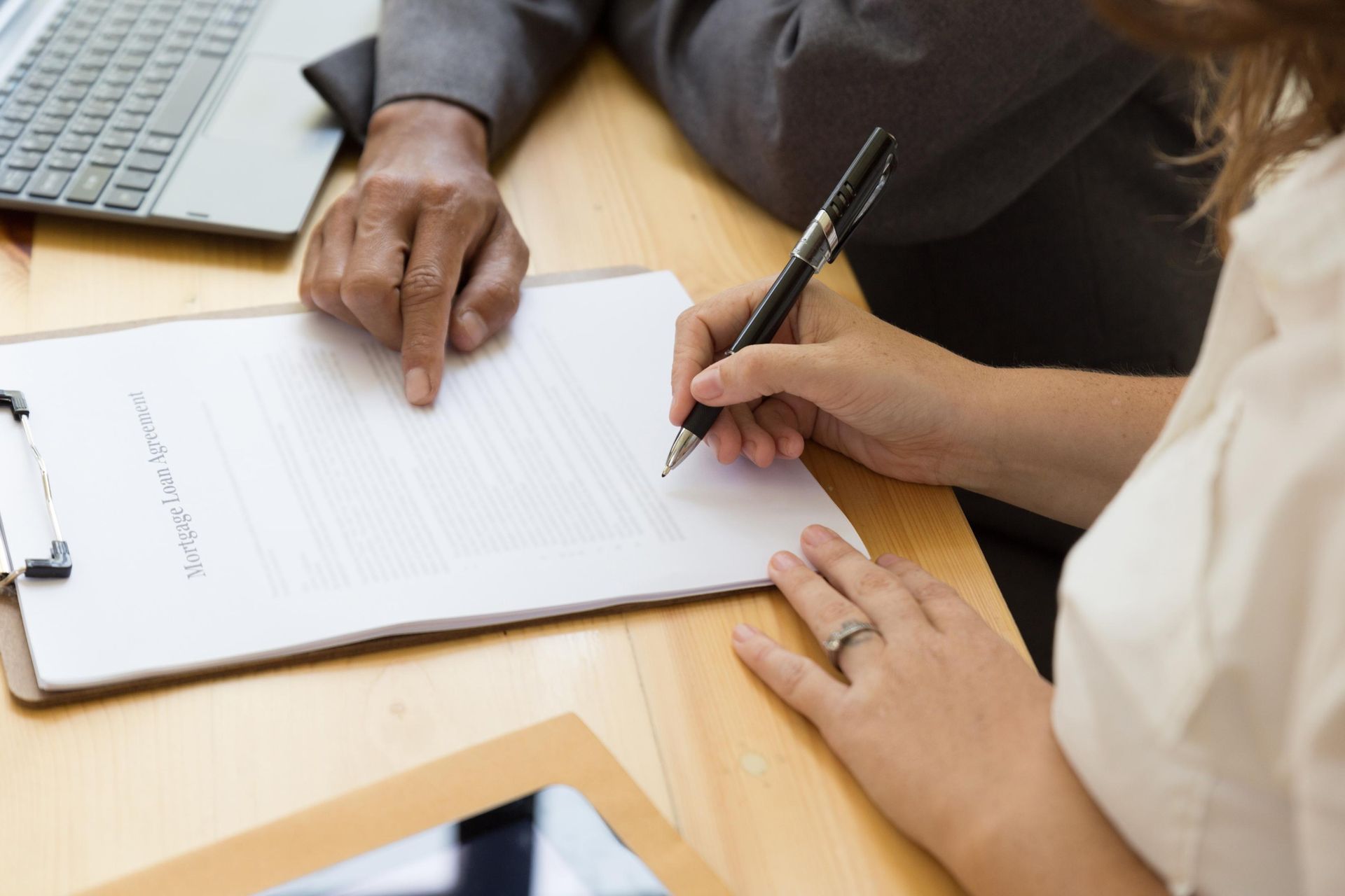 Two people signing a document at a wooden table, with a laptop nearby