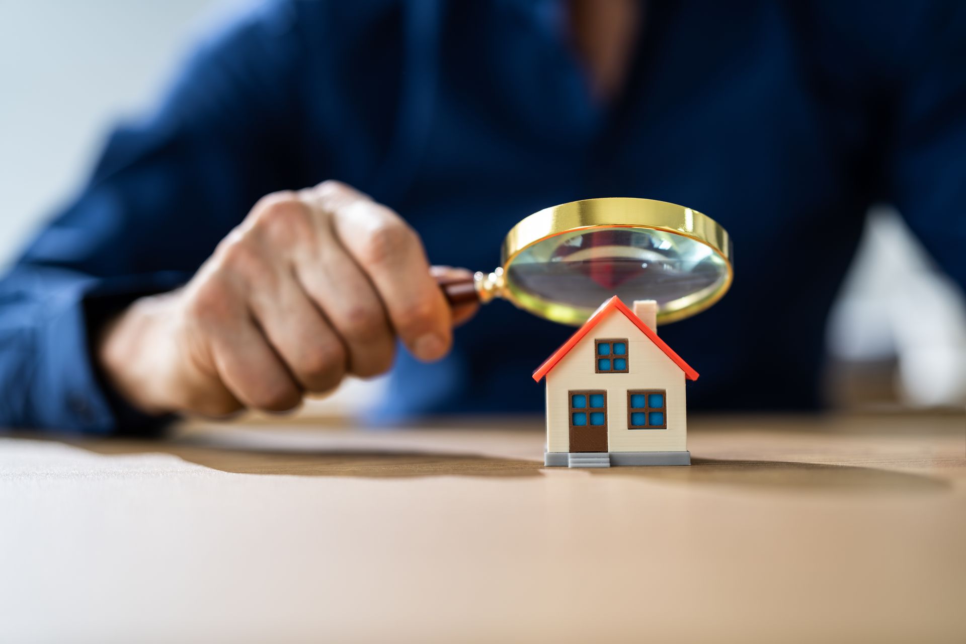 man holding magnifying glass pointing to mini house